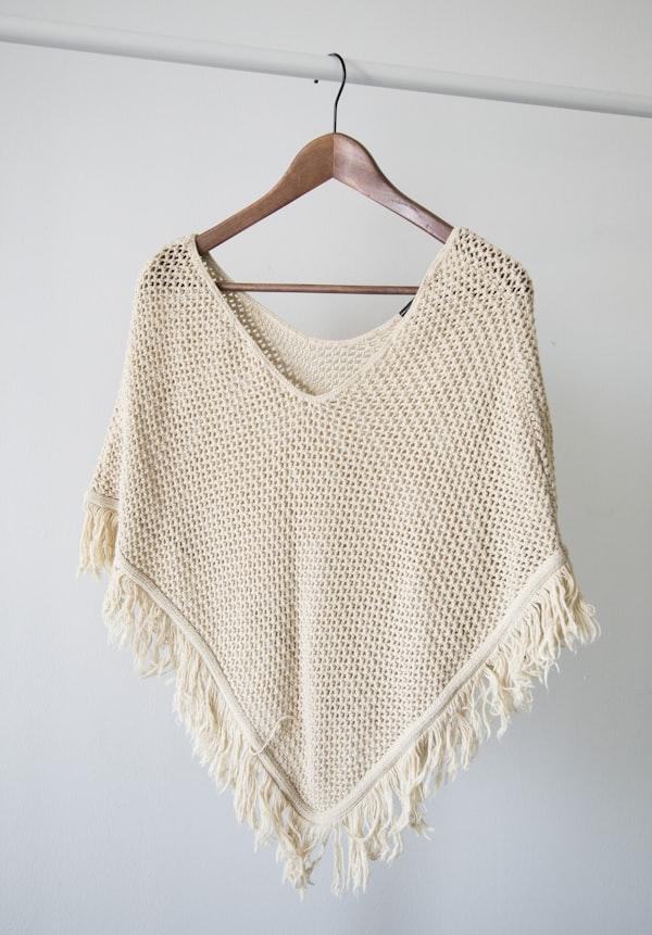 Blusa de tricô clara pendurada em um cabide de madeira.