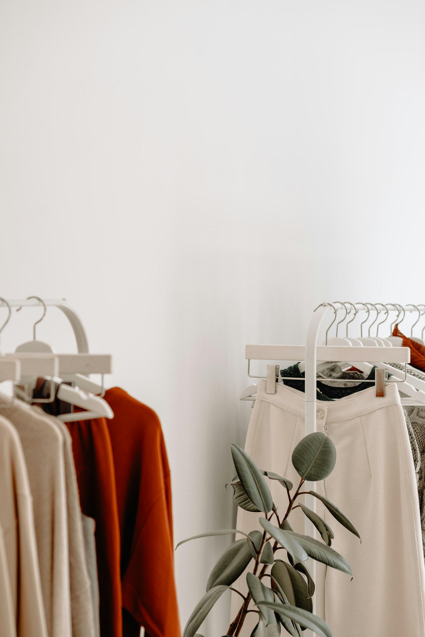 Arara com peças de roupa em tons neutros e claros, penduradas em cabides.